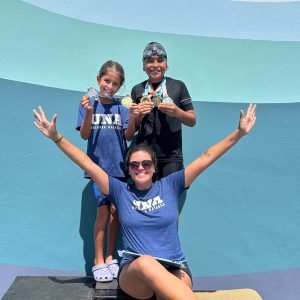 Em pé no Pódio, Guiovana Magalhães Silva ao lado de Enzo Souza juntos com a Auxiliar Maria Luiza - Foto: Divulgação/Pais dos atletas